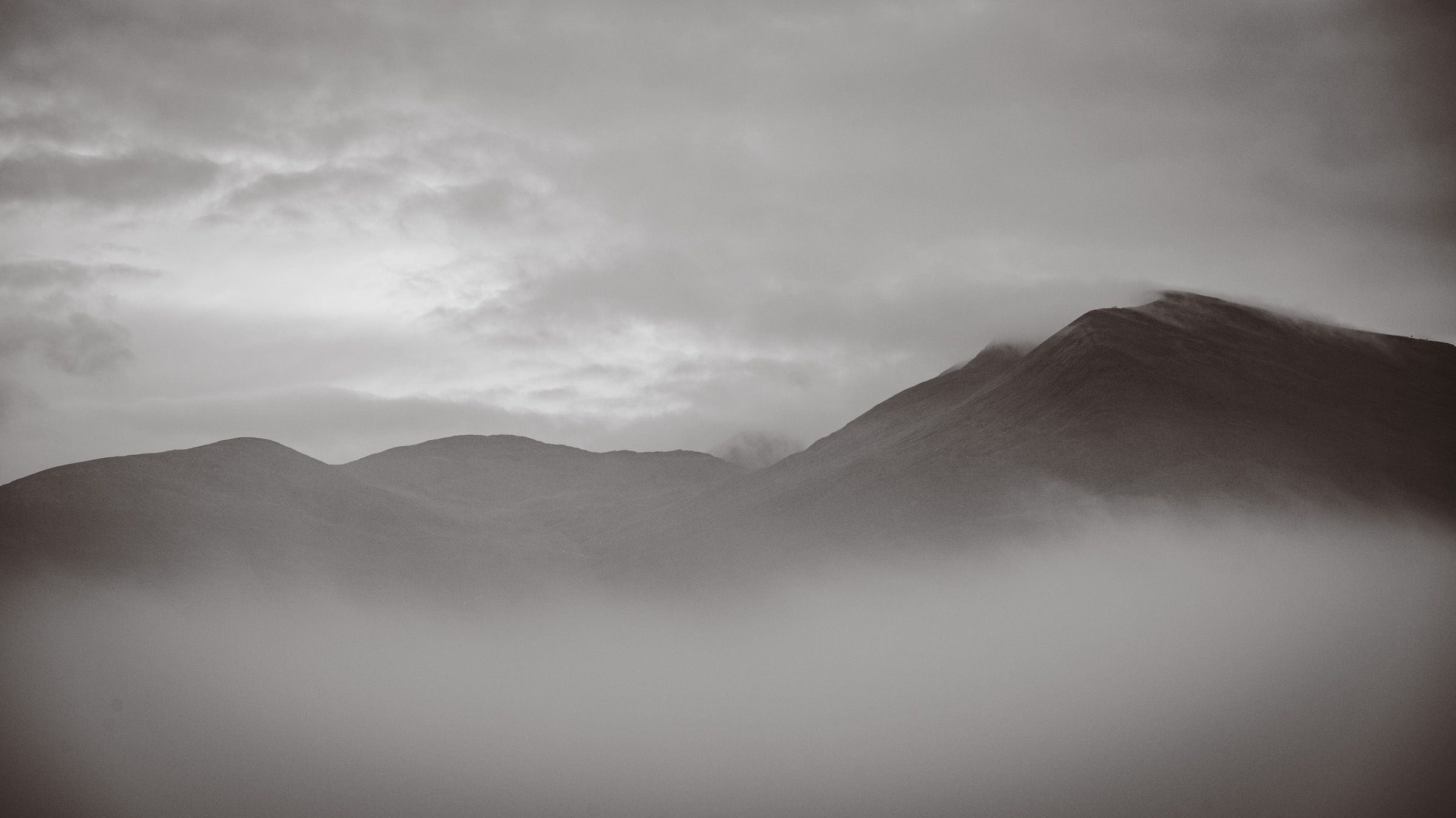 Black and white view of rounded mountains rising above a bank of mist
